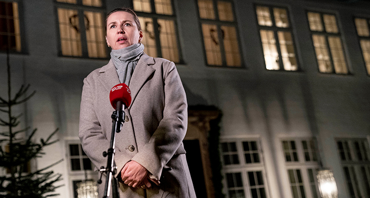 Mette Frederiksen står vid en mikrofon utomhus och pratar med journalister.