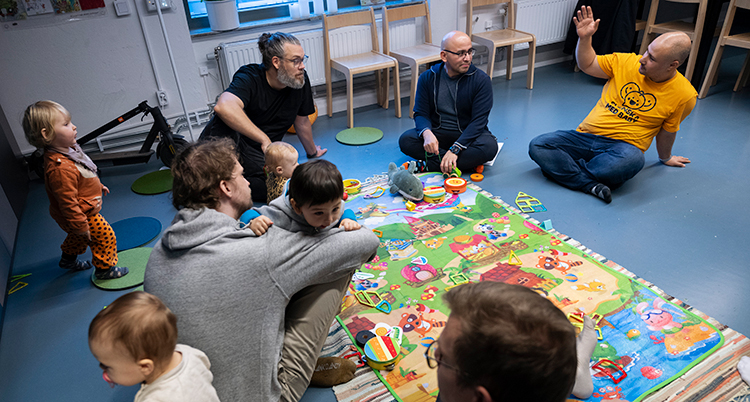 Pappor och barn sitter på ett golv och leker