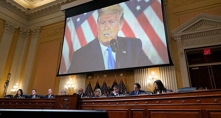 En rad poliitker sitter vid ett långt bord och pratar. Bakom dem syns en stor bild på Trump.