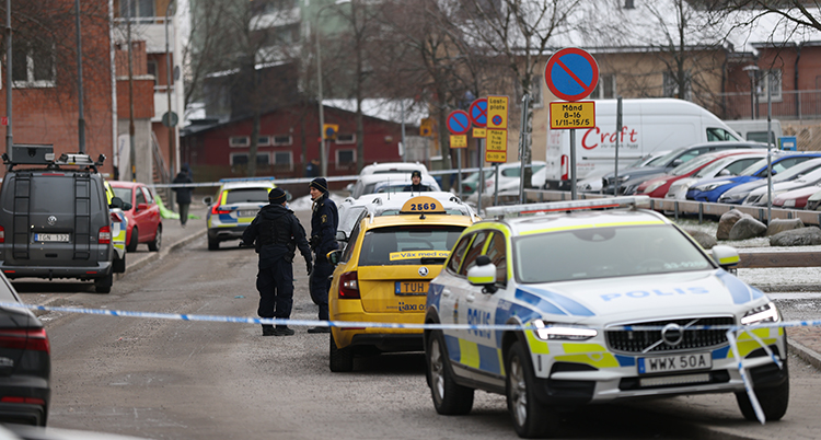 En polisbil och fler abilar är parkerad spå gatan. Poliser står i bakgrunden. Hyreshus syns i bakgrunden.