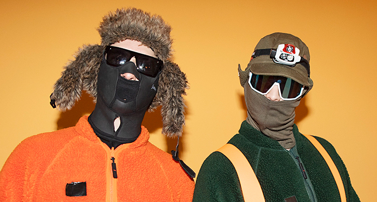 Två personer är vända mot kameran. De har solglasögon och masker på sig.