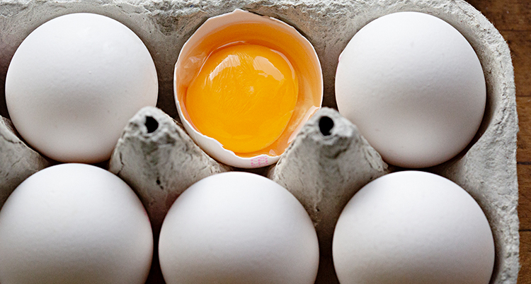 Sex ägg i en äggkartong. Ett ägg är knäckt.