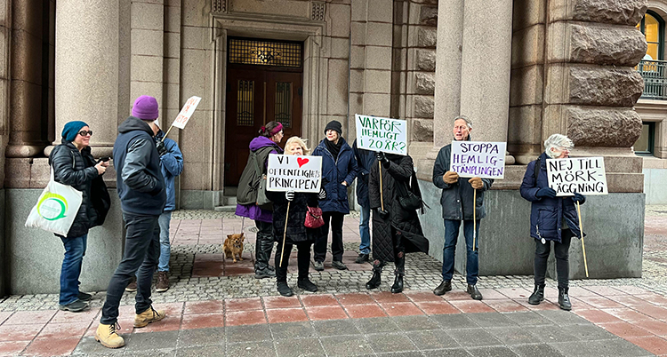 Några personer håller i skyltar utanför riksdagen.
