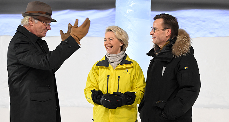 De står bredvid varandra ute. Det är snö bakom. De har tjocka jackor på sig.
