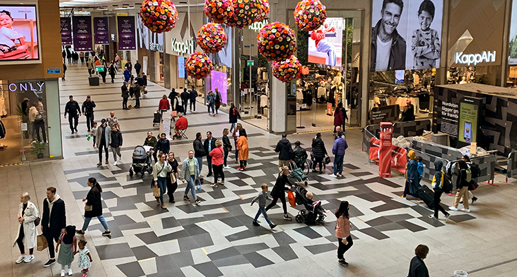 Många människor går runt i en stor byggnad. Många affärer syns.
