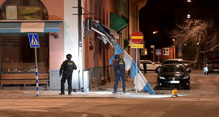 Poliser utanför huset på natten. En markis har förstörts och hänger från fasaden.