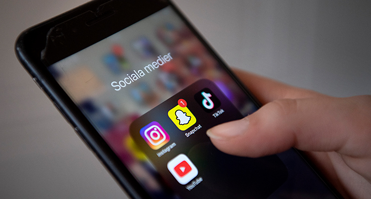En hand håller i en mobiltelefon med ikoner för sociala medier.