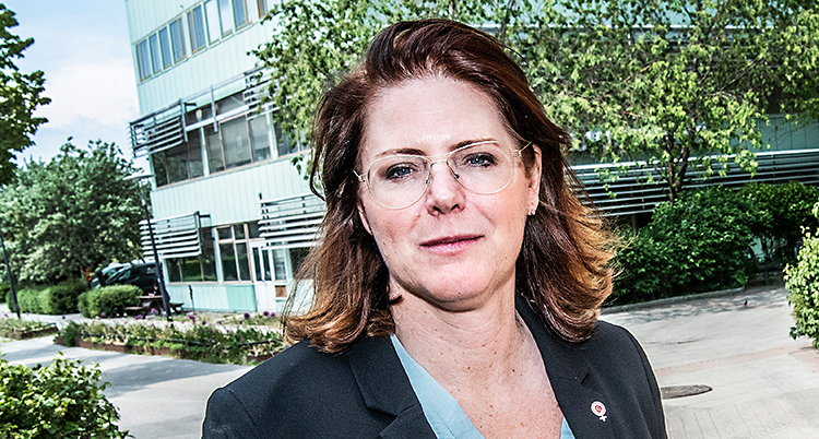 Hon står utomhus och tittar in i kameran.