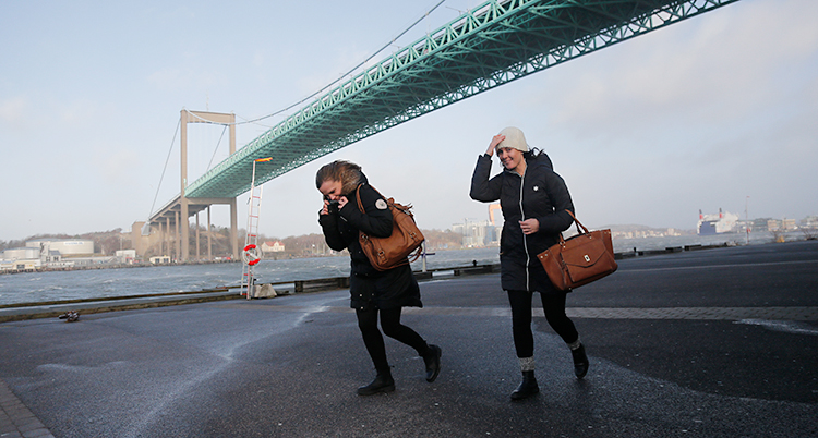 Två kvinnor går i blåsten nedanför Älvsborgsbron i Göteborg.