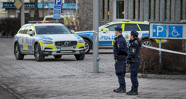 Två poliser och två polisbilar står på gatan utanför ett stort hus.