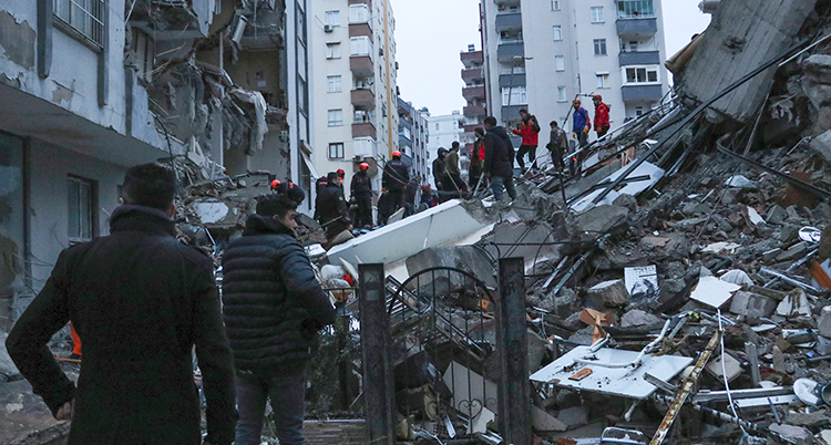 Ett rasat hus inne i en stad. Människor står på på det rasade huset.