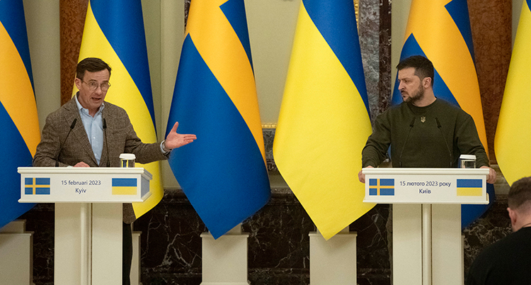 De står framför varsin mikrofon. Bakom sig syns ländernas flaggor i gult och blått.