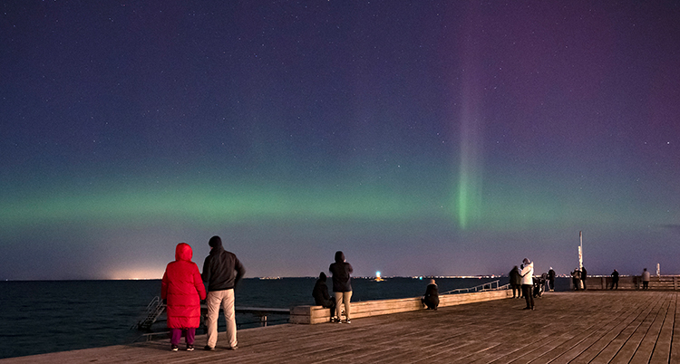 Folk står på en träbrygga och tittar på det gröna ljuset på himlen.