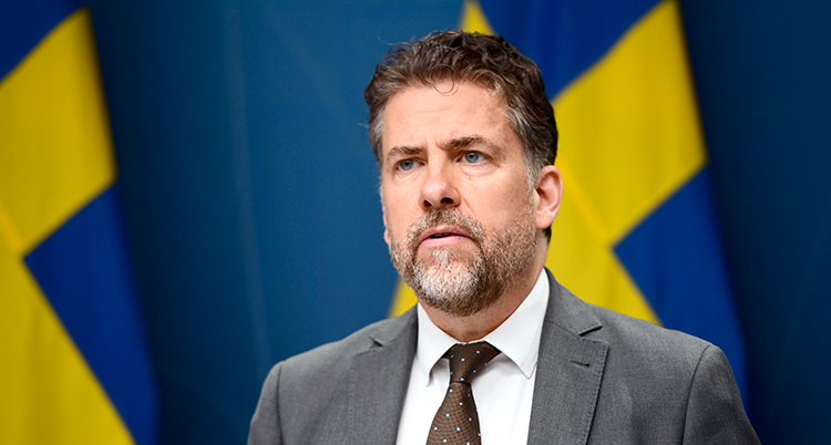 Han har slips. Bakom honom syns Sveriges flagga.