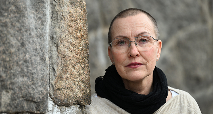 Hon står vid ett träd. Hon ser allvarlig ut.