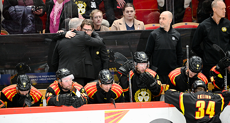 Spelare och tränare är i ett bås i en arena för ishockey. De ser ledsna ut.
