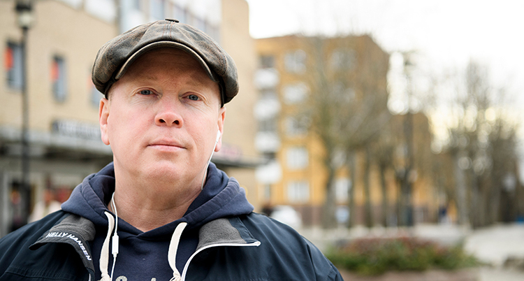 Han har vanliga kläder på sig och en keps.