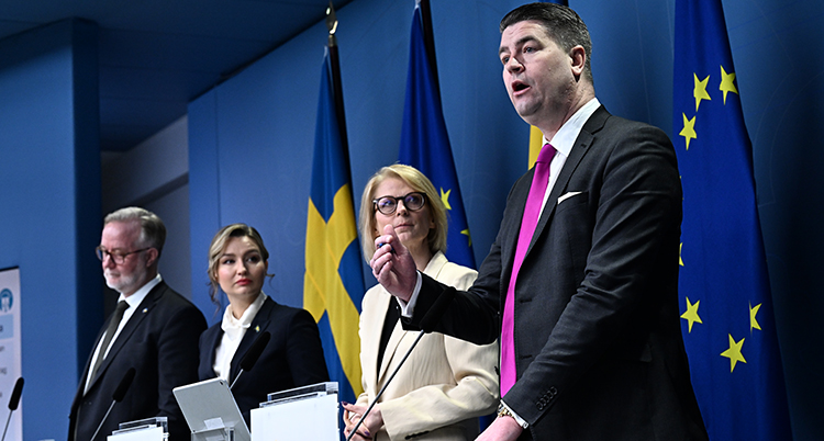 De står bredvid varandra bakom varsin mikrofon- Bakom är det blå flaggor.