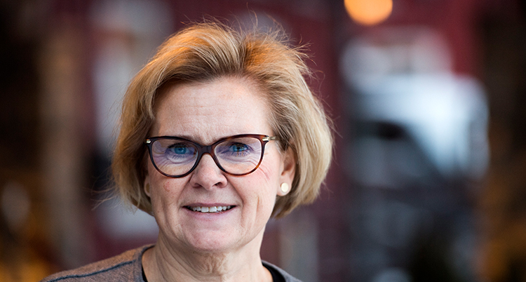 Hon har kort blont hår och glasögon.