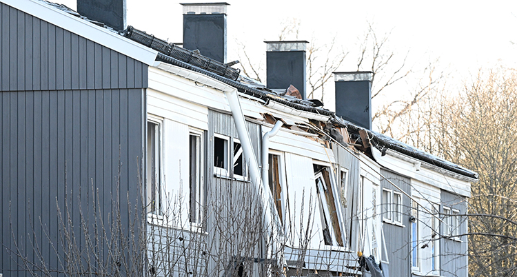 Ett gråvitt radhus i trä. Fasaden är trasig.