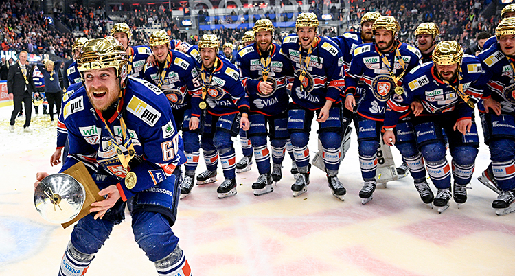 Glada ishockeyspelare som är på isen med guldhjälmar.