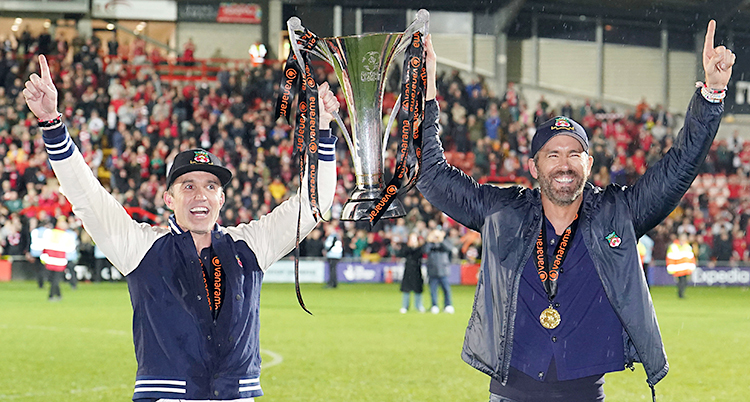 De står på en fotbollsplan och jublar. De håller i en pokal.
