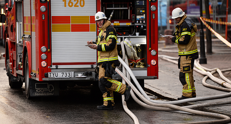 Två brandmän bakom en brandbil.