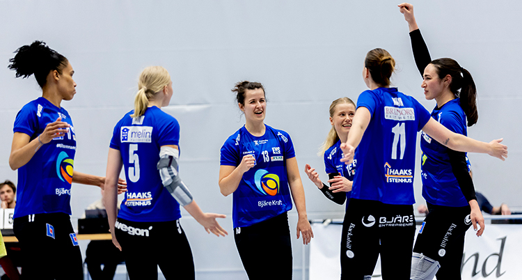 De har blå tröjor och står i en grupp. En sträcker upp en arm i luften.