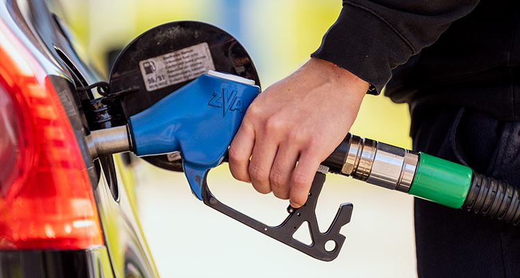 En person står och tankar en bil. Vi ser handen och en del av bilen.