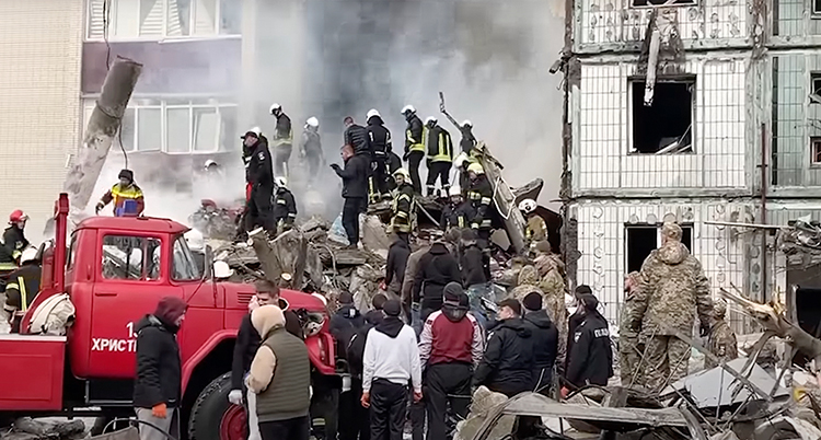 Människor står i bråte som rasat efter att ett högt hus delvis rasat ihop.
