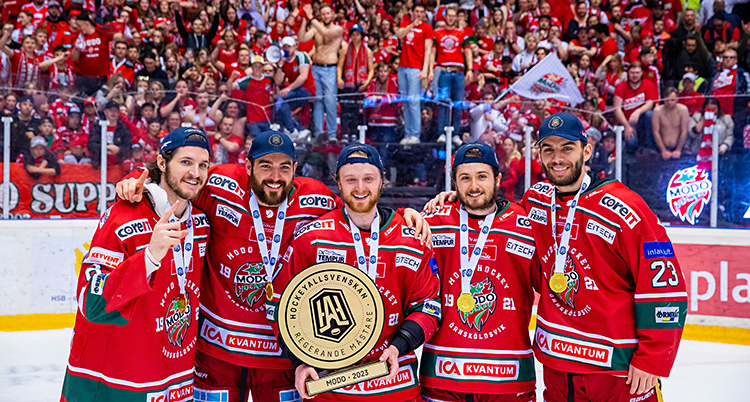 Några hockeyspelare står på isen och ser glada ut. Bakom dem är det fullt med folk på läktaren.