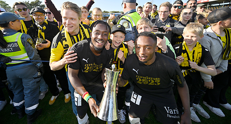 Några spelare håller i en pokal. De är glada och tittar in i kameran.