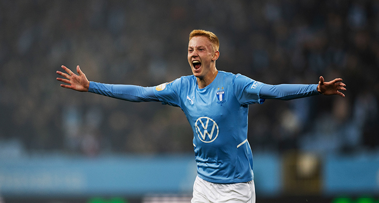 Han har blå fotbollströja. Han sträcker ut armarna och jublar.