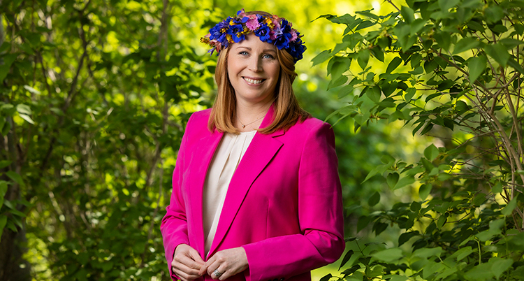 Annie Lööf ler mot kameran med en krans av blommor på huvudet.