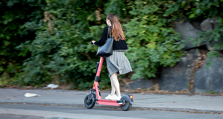 En tjej som åker på en elsparkcykel. Vi ser henne snett bakifrån.