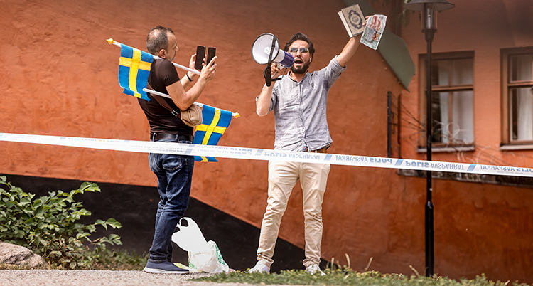 Två män bakom en avspärrning. En av dem håller en bok, den andra filmar.