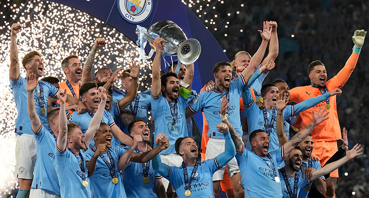 Laget står i en grupp och jublar. De har ljusblå tröjor. En hålla upp en pokal.