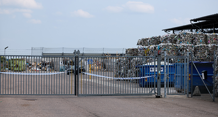 En avspärrad grind. Bakom grinden finns stora högar med plast.