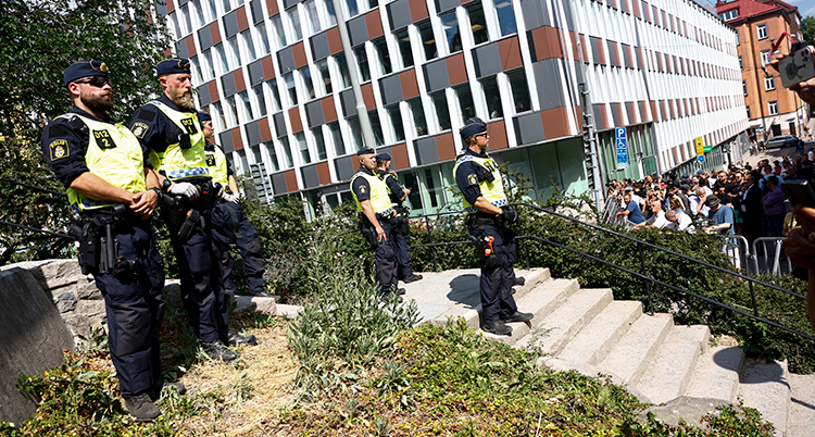 Poliser på en trappa utomhus framför personer som protesterar.