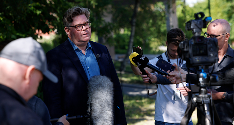 Ministern utomhus framför journalister.