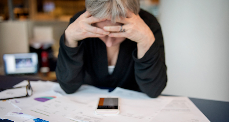En kvinna som ser ledsen och bekymrad ut. Hon sitter med sin mobil och med några räkningar.