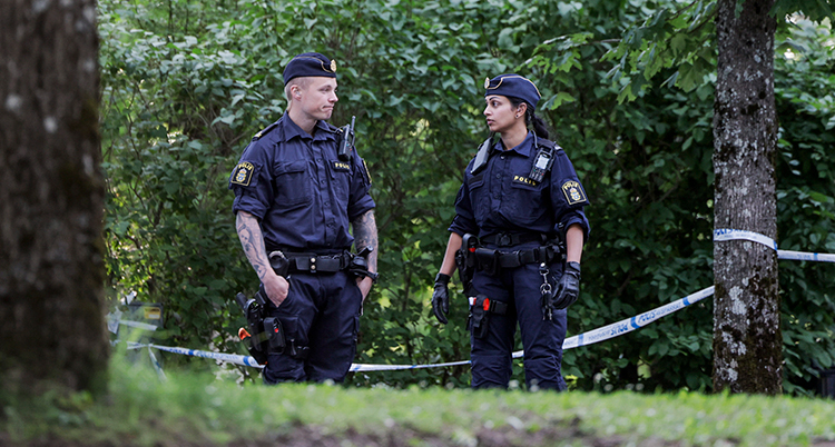 Två poliser framför träd och buskar och polisband.