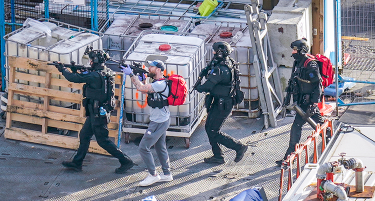 Fyra poliser med höjda gevär. En är civilklädd.