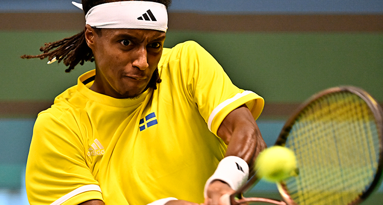 Han slår till en tennisboll med sitt racket.