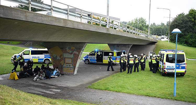 Tre polisbussar och massor av poliser. Poliserna har samlat ihop några personer som sitter på marken.