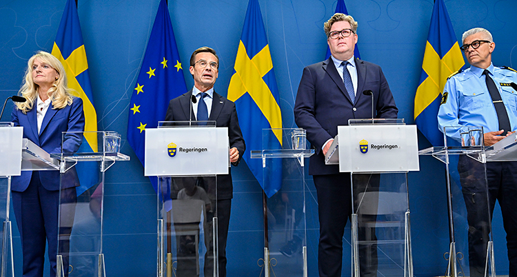 Fyra personer står bredvid varandra vid varsin talarstol med mikrofon.