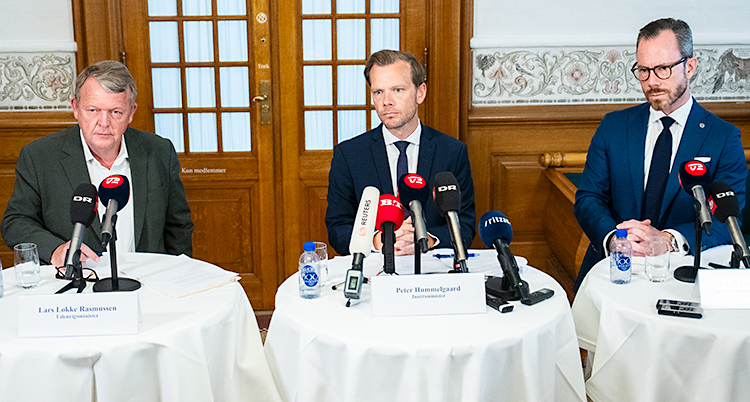 Tre män sitter vid några bord och pratar i mikrofoner.