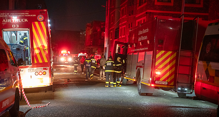 Det är kväll. Flera brandbilar och flera brandmän står på en gata i staden Johannesburg.