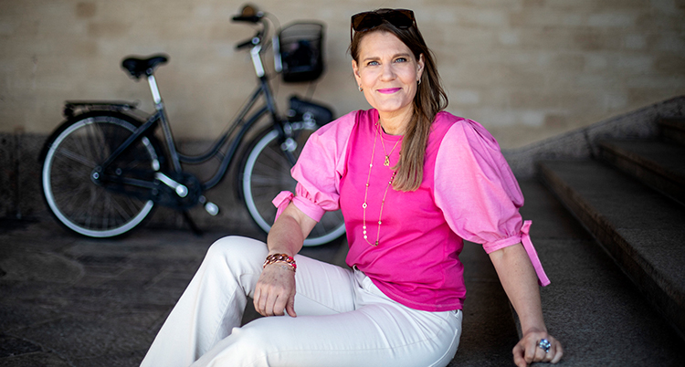Hon sitter ned. Bakom står en cykel lutad mot en vägg.