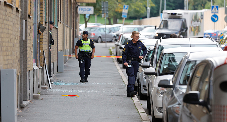 Poliser på en trottoar vid ett hus. Det ligger glassplitter på marken.